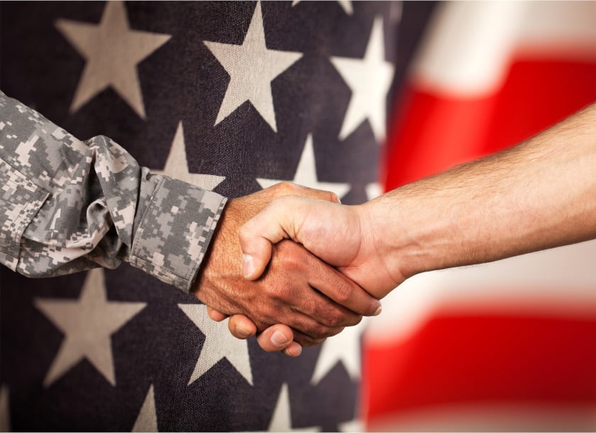 soldier and civilian shaking hands in front of an American flag